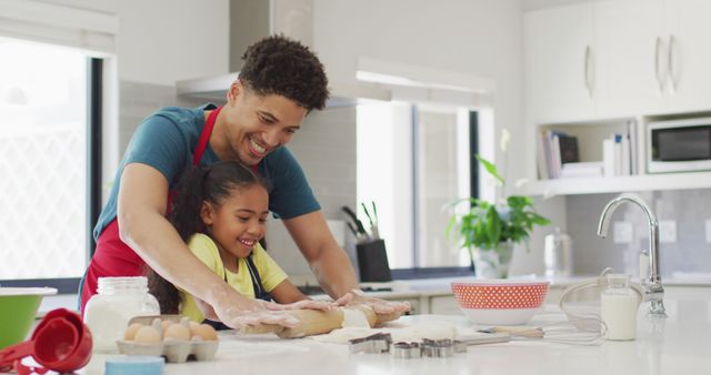Father and daughter enjoying baking together in a modern kitchen. Both are smiling while preparing dough. Perfect image for promoting family values, cooking classes, baking recipes, or kitchen appliance advertisements.