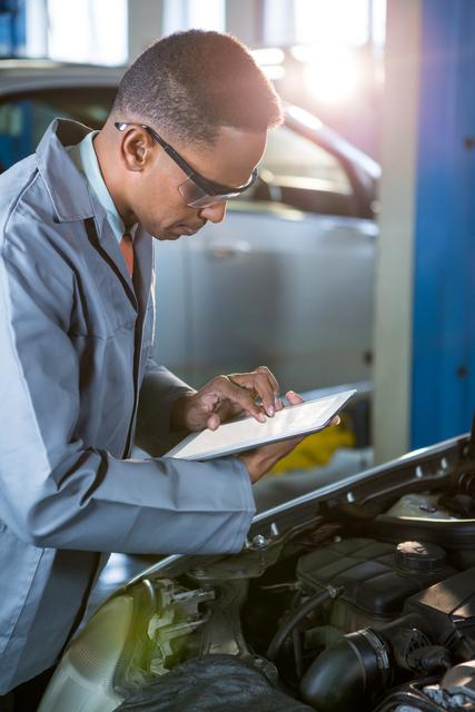 Mechanic using digital tablet for diagnostics in auto repair shop. Ideal for illustrating modern car maintenance, technology integration in automotive industry, and professional mechanic services.