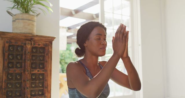Woman practicing meditation at home in bright room with natural light. Ideal for topics on mental wellness, relaxing environments, and mindfulness practices. Perfect for blogs, advertisements, or articles focusing on self-care, peaceful living, and home wellness routines.