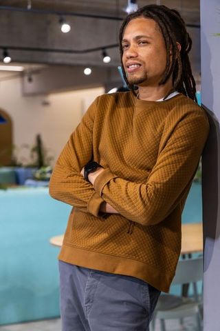 Relaxed african american man leaning in modern coworking lounge wearing brown pullover