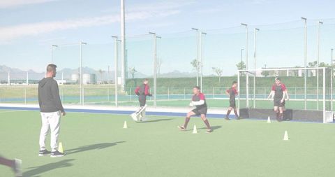 Male field hockey players practicing drills on synthetic turf with coach and goal