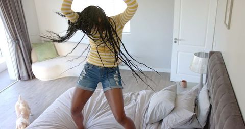 African american woman jumping on bed joyful energetic morning in sunlit modern bedroom