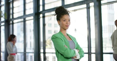 African american businesswoman standing confidently in glass atrium wearing green blazer