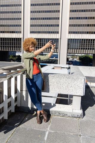African american woman taking selfie on urban rooftop balcony in sunlight
