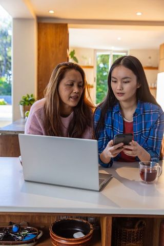 Asian Mother and Daughter Bonding Over Technology in Modern Kitchen