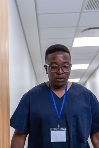 African american healthcare worker standing in clinic corridor wearing navy scrubs and badge