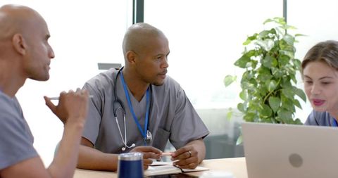 African american clinicians collaborating over notes and laptop in bright clinic meeting