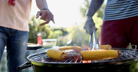 Two Young Men Grilling Corn and Patties in Backyard Gathering
