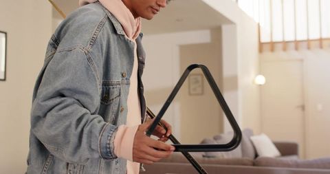 Young musician playing triangle in modern living room with denim jacket and relaxed vibe