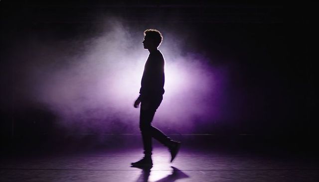 Backlit silhouette walking through purple haze on stage with dramatic rimlight