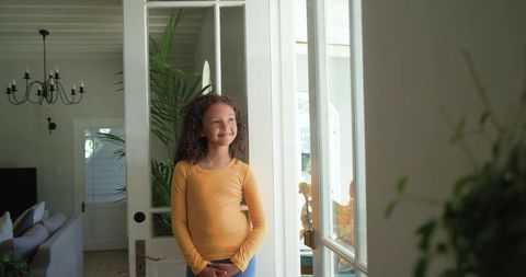 Sunlit girl standing in doorway smiling and daydreaming while wearing yellow top
