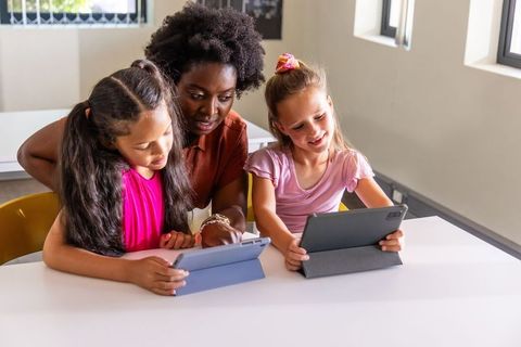 African american teacher guiding two school girls using tablets for collaborative learning