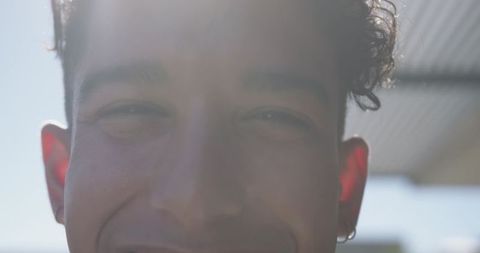 Sunlit close-up showing smiling young man squinting with hoop earring and lens flare
