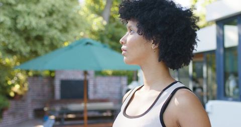 Contemplative african woman standing in sunlit patio profile wearing casual tank top hoop earring