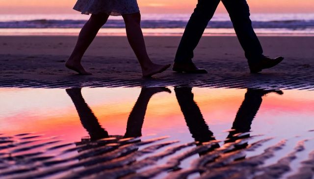 Couple walking on beach at sunset with vibrant tide pool reflection