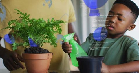 Boy watering potted fern with spray bottle while caregiver guiding indoor gardening