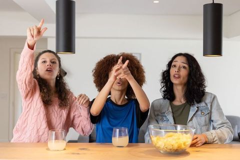 Diverse friends cheering during game night with chips and drinks at modern kitchen table