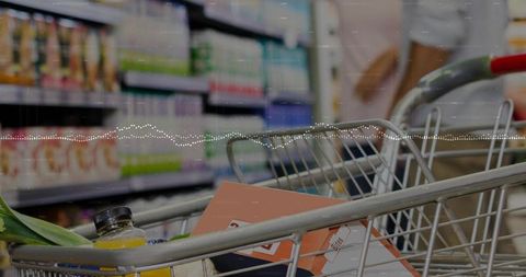 Couple pushing grocery cart with leek, juice bottle and boxed goods in supermarket aisle