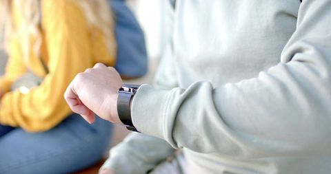 Checking Rectangular Smartwatch on Wrist in Casual Lounge with Diverse Adults wearing green sweatshi