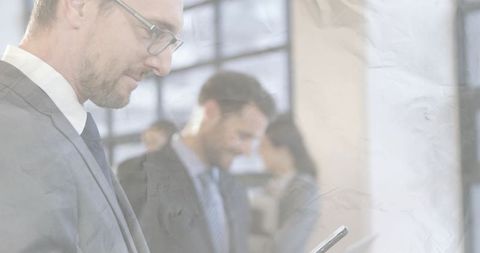 Executive checking smartphone in modern office with blurred colleagues and grid windows