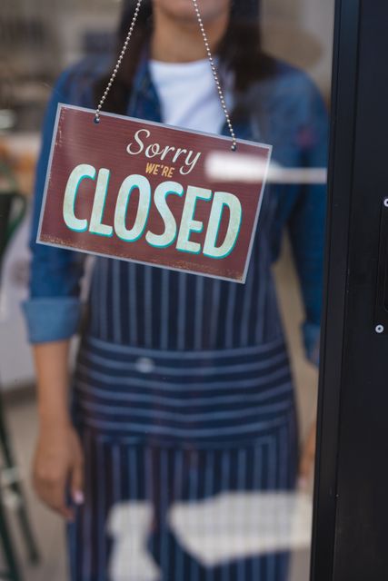 Close-up of closed signboard on door with biracial young female owner standing in background. unaltered, text, cafeteria, barista, occupation and small business concept.