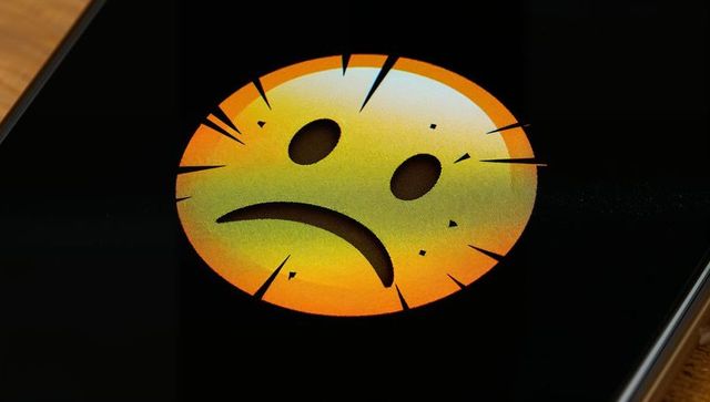 Displaying cracked sad emoji on smartphone screen closeup showing shattered emoticon