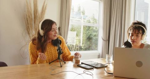 Recording cozy home podcast with two hosts, microphones, headphones and laptop