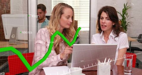 Two women collaborating over laptop pointing at green growth chart showing business analytics