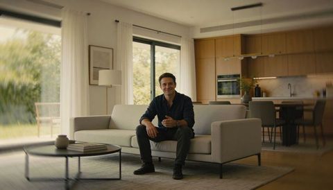 Smiling Man Sitting on Modern Gray Sofa in Minimalist Open Plan Living Room in Warm Daylight