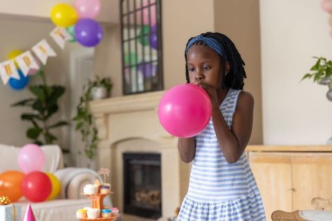 Young african american girl blowing pink balloon home birthday party cupcakes pastel decor