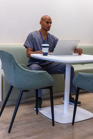 African american healthcare professional working on laptop in staff lounge with coffee