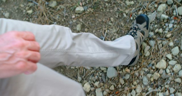Man hiking on outdoor rocky trail wearing beige pants and black hiking shoes. Ideal for use in travel blogs, outdoor adventure promotions, hiking gear advertisements, or nature expedition articles.