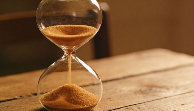 Golden sand flowing through glass hourglass on rustic wooden table with warm glow