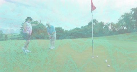 Senior golfer lining up putt on green while companion gesturing near flagstick and three balls