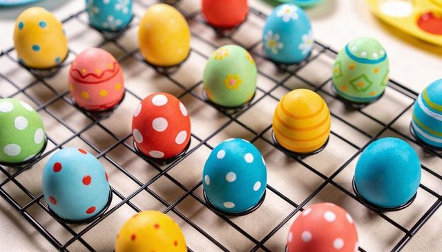 Colorful hand-decorated easter eggs with polka dots and stripes resting on black drying rack