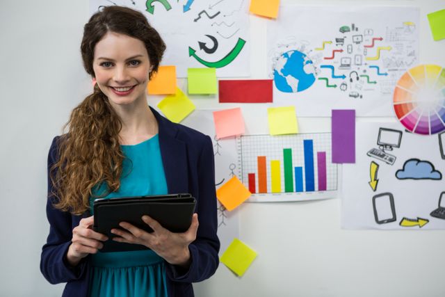 Smiling woman holding digital tablet standing in front of a wall covered with colorful charts, graphs, and brainstorming notes. Ideal for use in business, technology, and creative industry contexts, showcasing modern workplace environments, teamwork, and innovation.