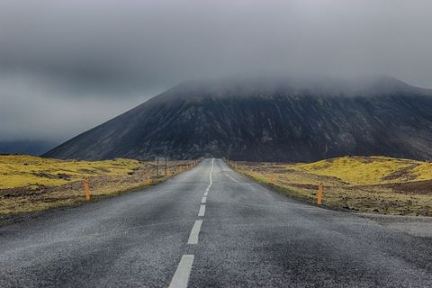 Endless road leading to fog-shrouded volcanic mountain over mossy lava fields