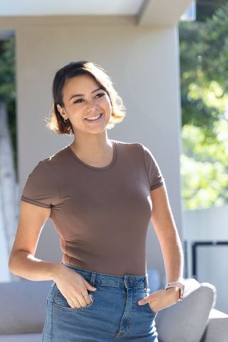 African american woman smiling on sunlit porch wearing denim jeans and smartwatch