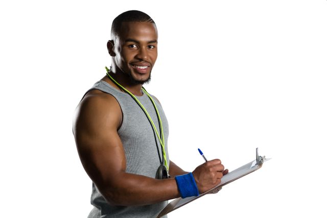 Portrait of smiling male rugby coach writing on clipboard while standing against white background