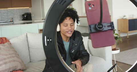 African-american man vlogging on couch with ring light and red smartphone, content creator