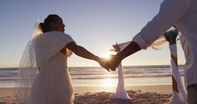 African american couple in love getting married, holding hands on the beach at sunset. marriage, love and romance, holiday by the sea.