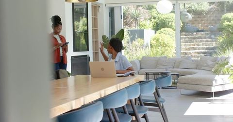 African mother working from home with teenage daughter using phone in bright modern lounge