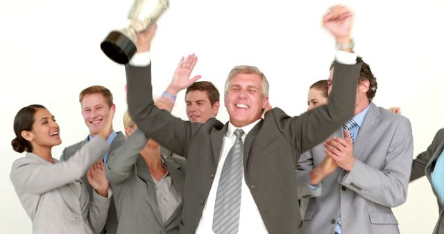 A diverse group of businessmen and businesswomen celebrate a victory or success, with a middle-aged man in the foreground holding a trophy aloft. Their expressions of joy and accomplishment suggest a team achievement in a corporate or competitive setting.