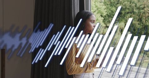 Woman gazing out window holding smartphone with digital waveform overlay, lifestyle