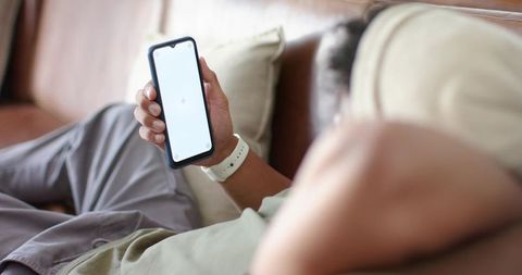 African american man reclining on sofa holding smartphone with blank screen wearing white watch