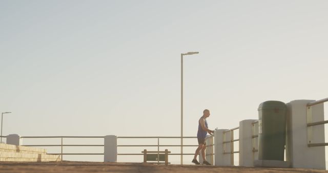 Man seen jogging near ocean promenade during sunrise. Ideal for promoting healthy lifestyle, fitness routines, or outdoor exercise campaigns. Image captures sense of serenity and dedication.