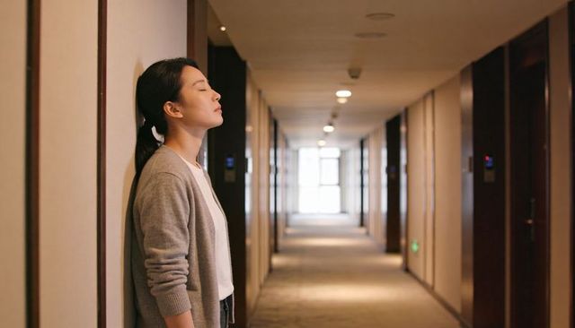 Contemplative young woman leaning against hotel corridor wall, calm pause and solitude