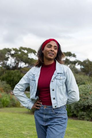 Indian woman standing confidently in park wearing denim jacket and red headband
