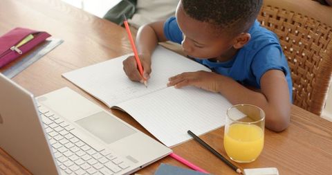 African american child studying at wooden desk with laptop, writing homework