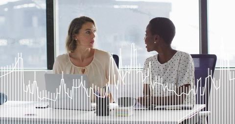 Two colleagues discussing analytics and reviewing data on laptop with graphs overlay in modern offic